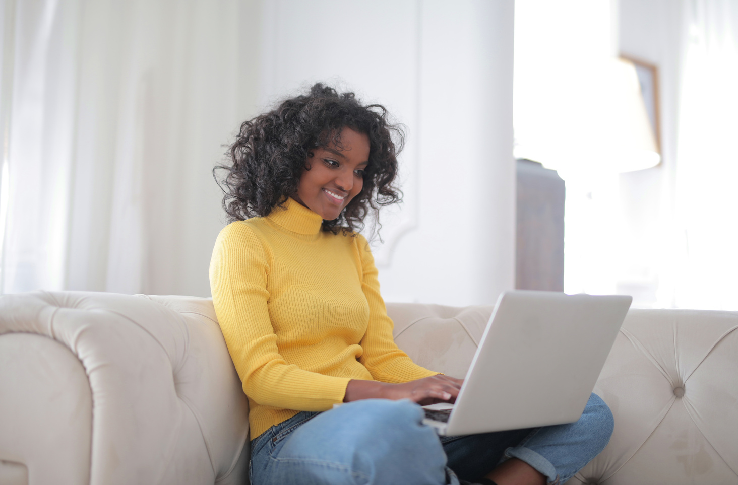 Positive young ethnic lady working on laptop while sitting at couch at home